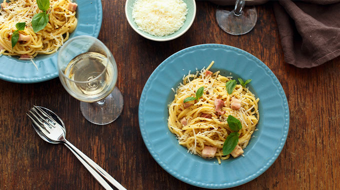 A glass of white wine served with pasta carbonara.