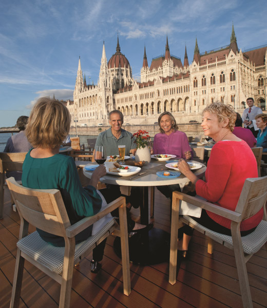 Viking passengers dining on outdoor terrace of ship with the Hungarian Parliament Building in the background.