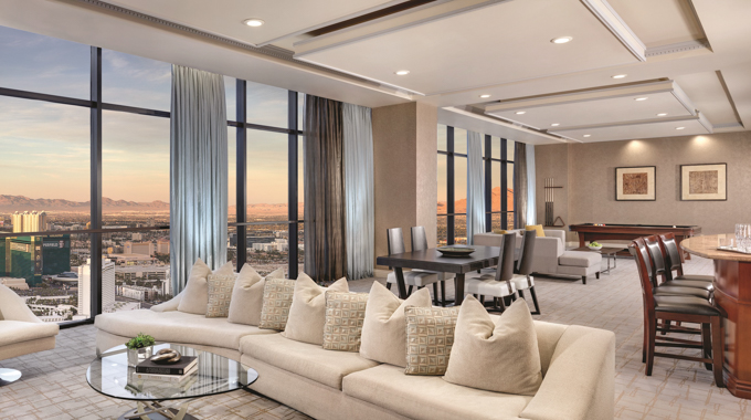 Suite living area with various seating and floor-to-ceiling windows running the length of the room