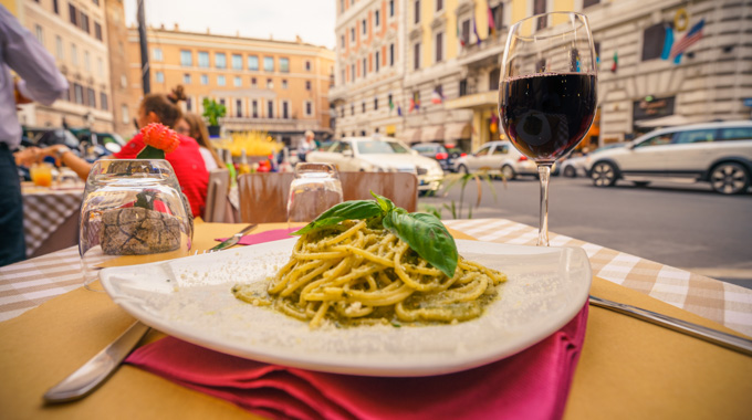 A plate of pesto pasta and a glass of red wine served al fresco