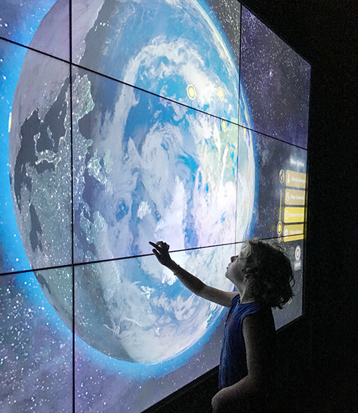 Child touching a screen showing an interative image of the earth.