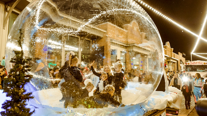 Woman and young children wave from inside a snow globe parade float.