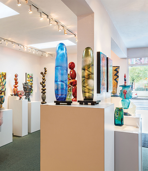 Glass art pieces displayed on pedastals inside a gallery.