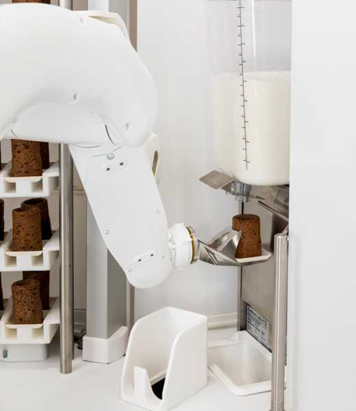Robot arm holding a Cookie Shot under a milk dispenser