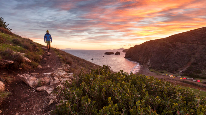 A hiker on a trail above Scorpion Beach at sunset