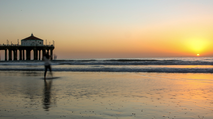 A skimboarder in the water at Manhattan Beach during sunset.