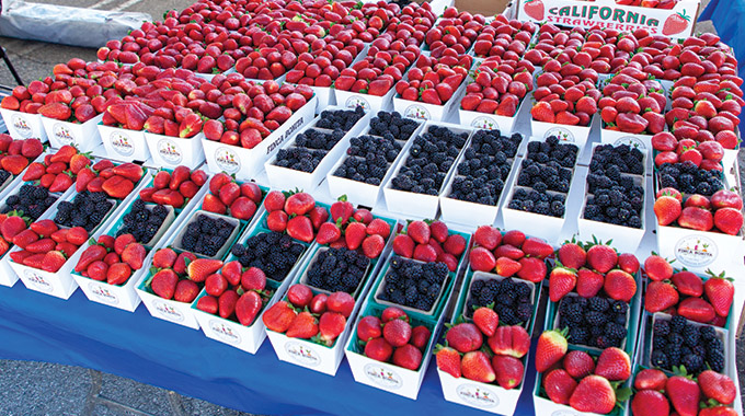 A table filled with baskets of strawberries, blackberries, and blueberries
