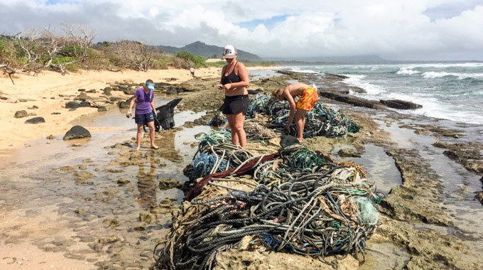 A trio of people cleaning up ropes and other debris from a beach.