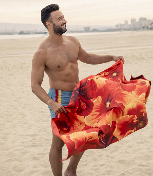 Man on the beach holding a hibiscus-print towel.