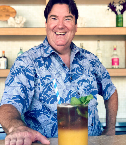 James Shoemaker sitting behind the bar, a cocktail in front of him