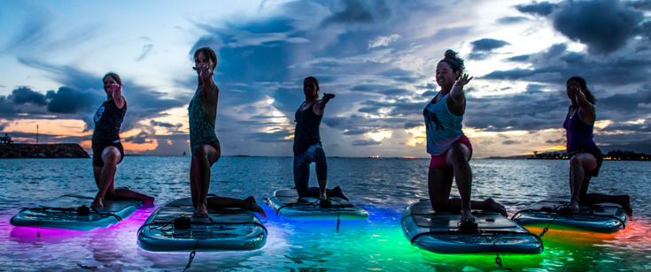 A group of yogis balancing on paddleboards while holding a yoga pose.