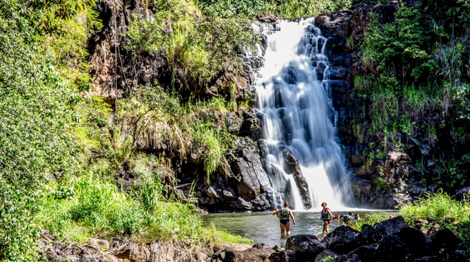 People swimming at the base of a waterfall