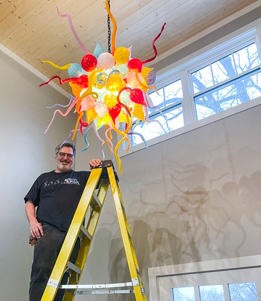 James Hayes on a ladder underneath a chandelier he created.