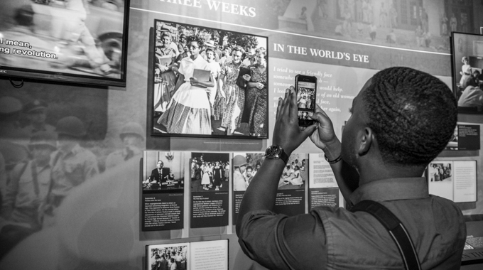 A visitor taking a picture on his phone of an old image displayed at the Little Rock Central High School National Historic Site