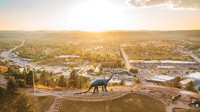 Dinosaur statue silhouetted against a sunny Rapid City sky.