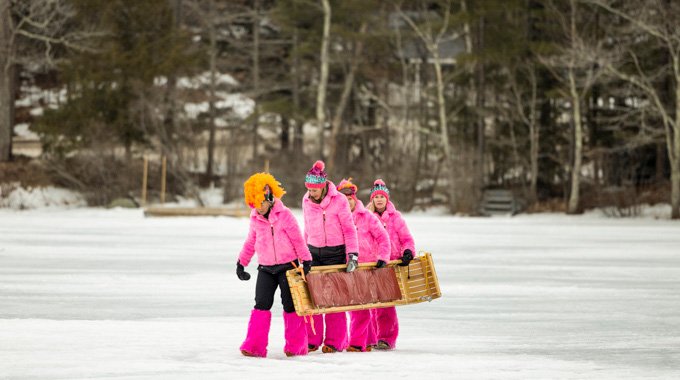 Four people in matching pink outfits carrying a toboggan.