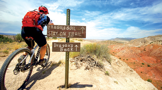 Biker riding past a sign pointing toward Dragon's Back and warning riders of fragile soil