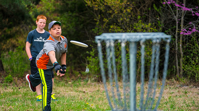 Boy playing disc golf throwing a disc toward a basket.