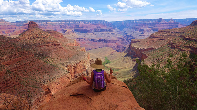 A hiker sits at the edge of a rockface in Grand Canyon National Park