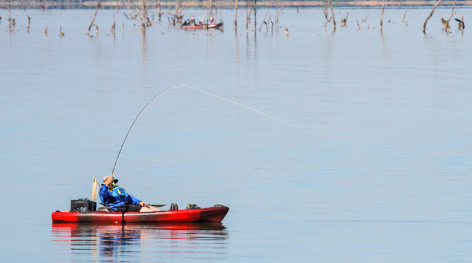 A fisherman drawing up his line while sitting in a red canoe