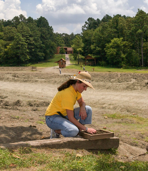 A woman picking through a container of soil in search of diamonds