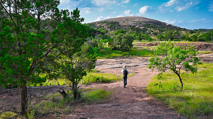 A hiker heads towards the batholith, a pinkish dome that's the main attraction at Enchanted Rock State Natural Area near Fredericksburg. | Photo by Jonathan–stock.adobe.com