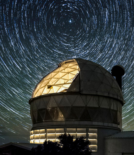 McDonald Observatory illuminated at night, with stars swirling overhead