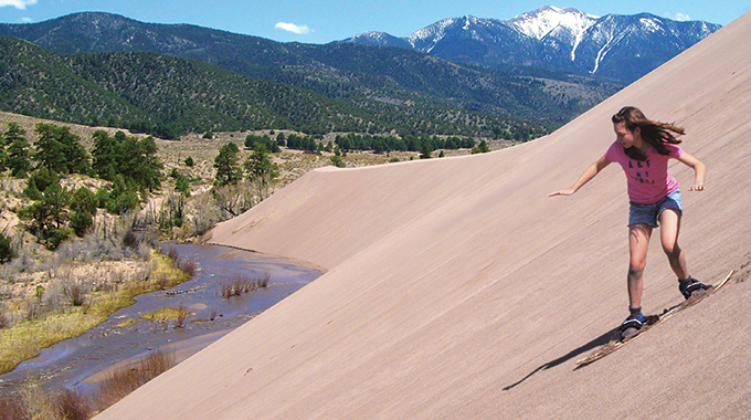 A child enjoys sand sledding at Great Sand Dunes National Park. | Photo by Patrick Myers/NPS