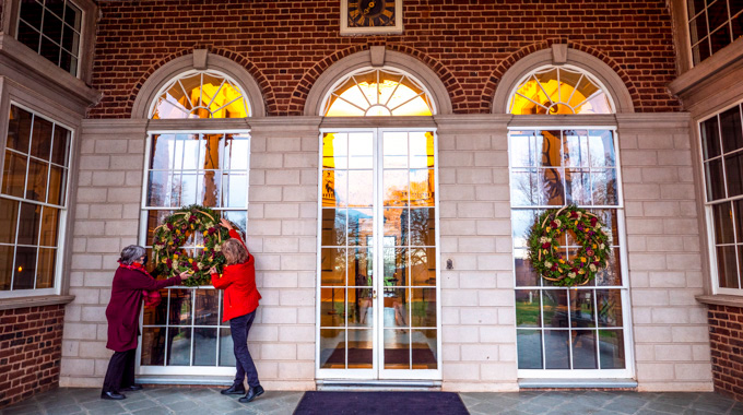 Two women hanging a wreath on a window at Monticello