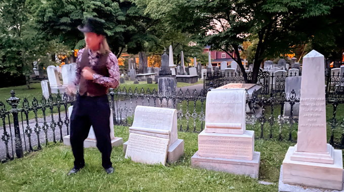 Tour guide standing beside headstones in a cemetery. 