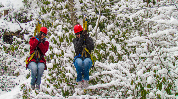 Two people ziplining among snow-covered trees
