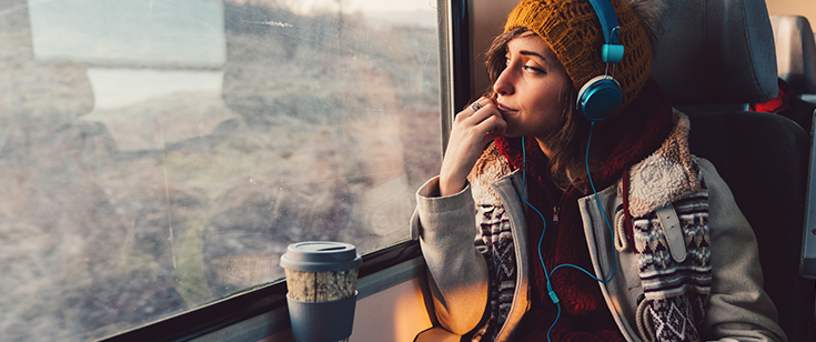 Woman listening to headphones while looking out a train window Woman listening to headphones while looking out a train window