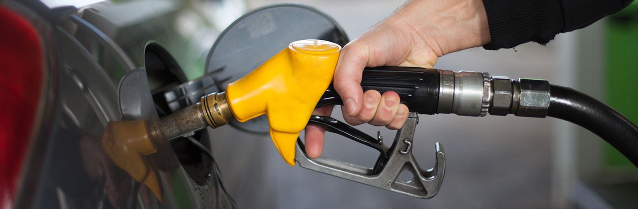 A hand holds a yellow gas pump fueling a car
