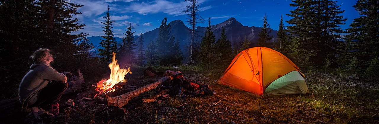 Man looking up at stars next to campfire and tent at night