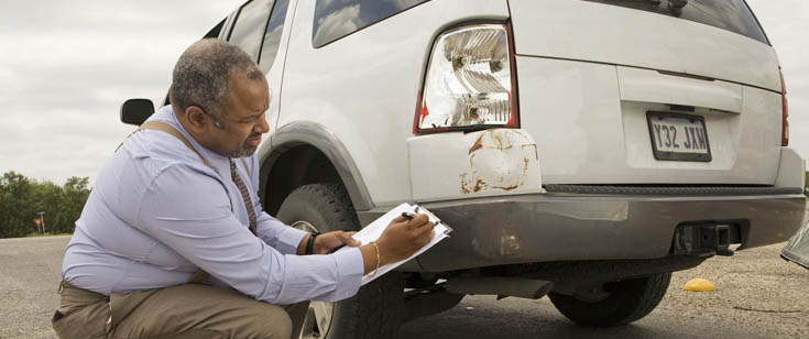 Claims agent taking notes while inspecting a damaged vehicle Claims agent taking notes while inspecting a damaged vehicle