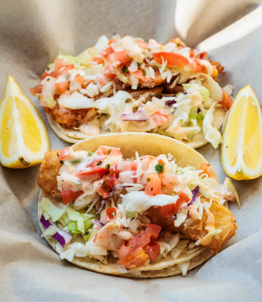 A pair of Hook’d Fish Grill tacos with lemon wedges.