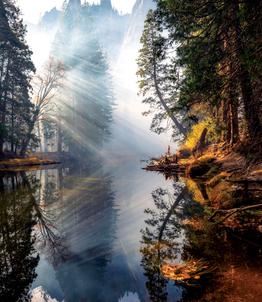Yosemite Grandeur by Jared Weintraub, showing sunrays highlighting a hiker standing beside a river.