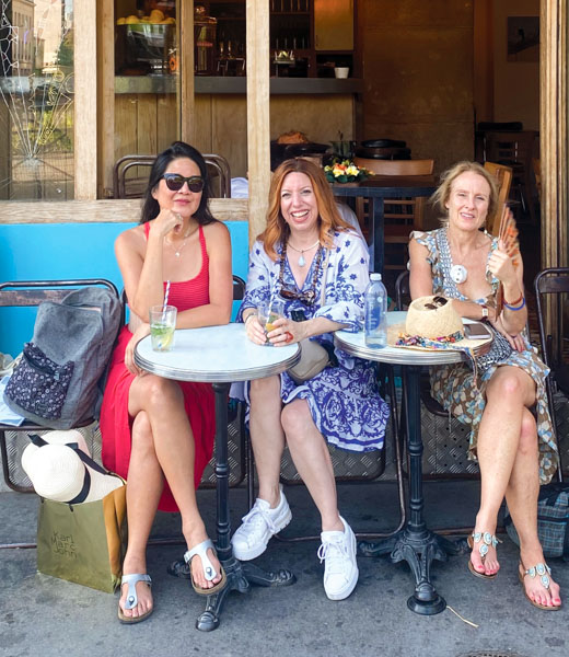 Three women sharing drinks al fresco at a bistro.