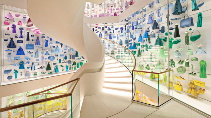 A rainbow of clothing and accessories inside glass display cases surrounding a spiral staircase in the Christian Dior Museum.