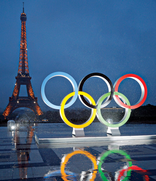 Olympic rings on the Trocadero esplanade, with the Eiffel Tower aglow in the distance.