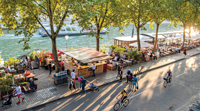 Pedestrians, cyclists, and diners fill the path beside the Seine.
