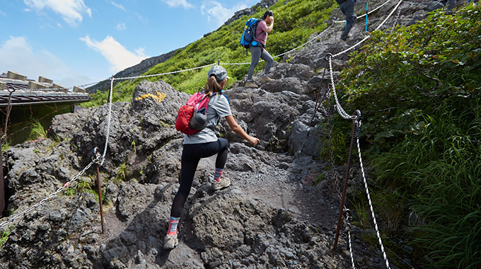 Hikers use ropes and hands and feet to scramble up large rocks on the path to the top of Mount Fuji, Japan