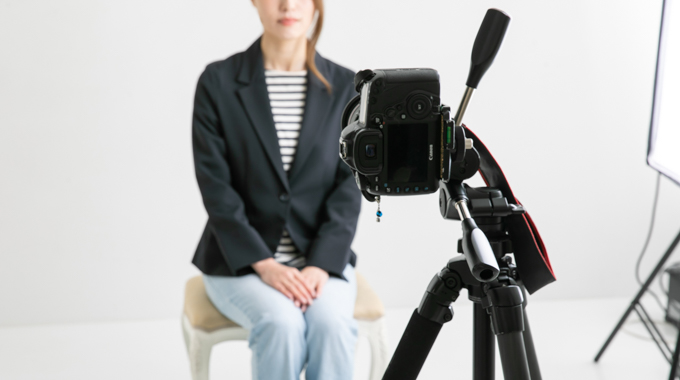 A woman seated in front of a digital camera on a tripod.