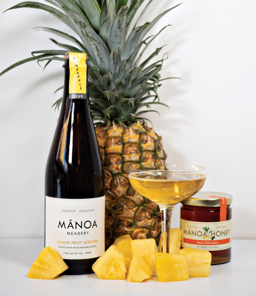 A glass of pineapple mead from Manoa Honey & Mead, arranged with chunks of fresh pineapple 
